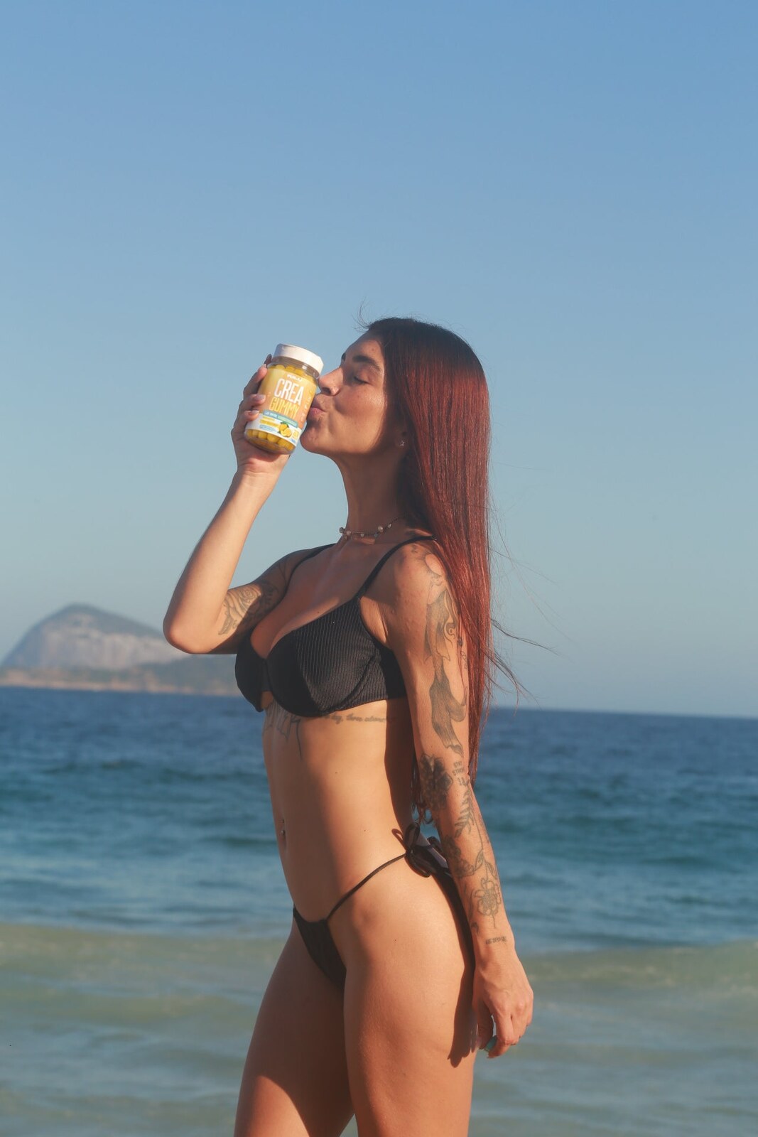 Mulher na praia beijando o pote de Creatina Gummy limão