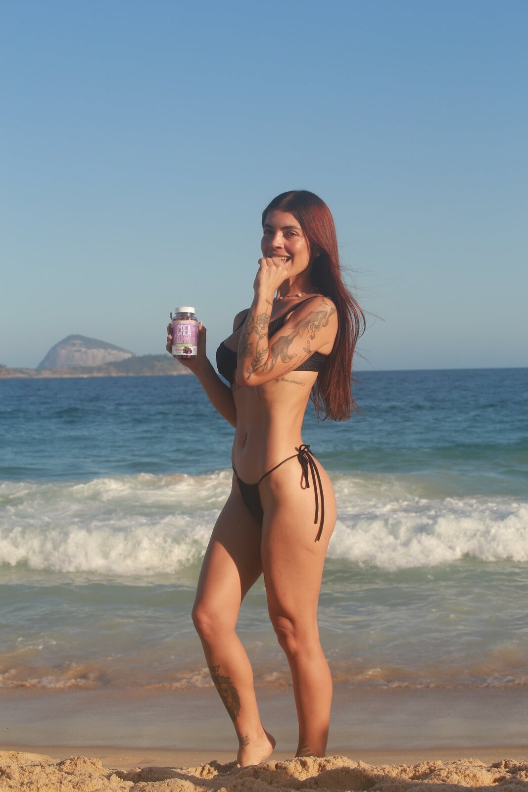 Mulher na praia com o pote de Creatina Gummy uva