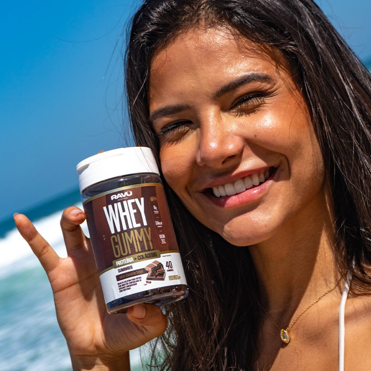 Modelo na praia com o Whey Gummy RAVU Chocolate